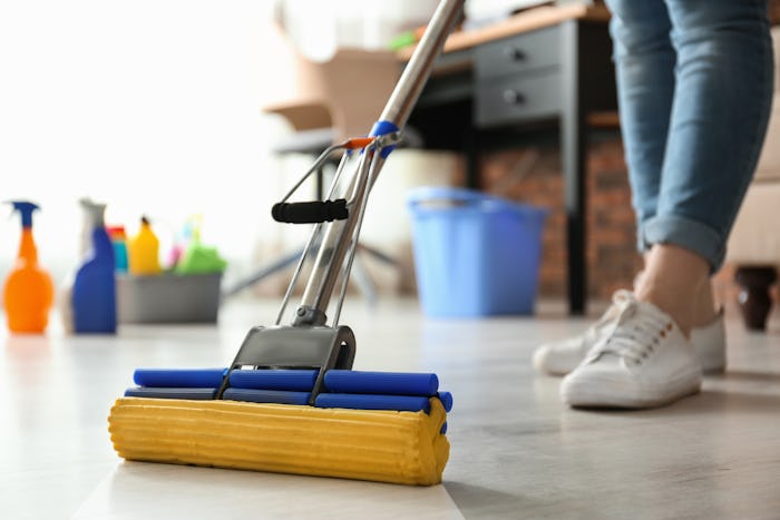 Woman cleaning floor with mop in living room for flu season