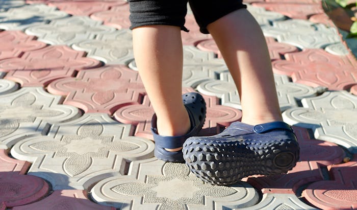 Small boy wearing blue rubber Crocs sandals outdoors.
