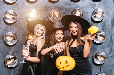 Picture of three emotional young women in halloween costumes on party with pumpkin.