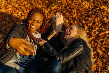 very happy female friends making funny selfie in autumn park. Cute girls with different colored skin...