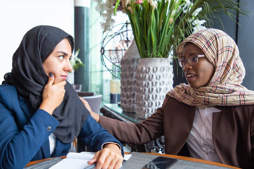 Serious African American employee supporting colleague. Muslim businesswomen chatting in coffee shop...