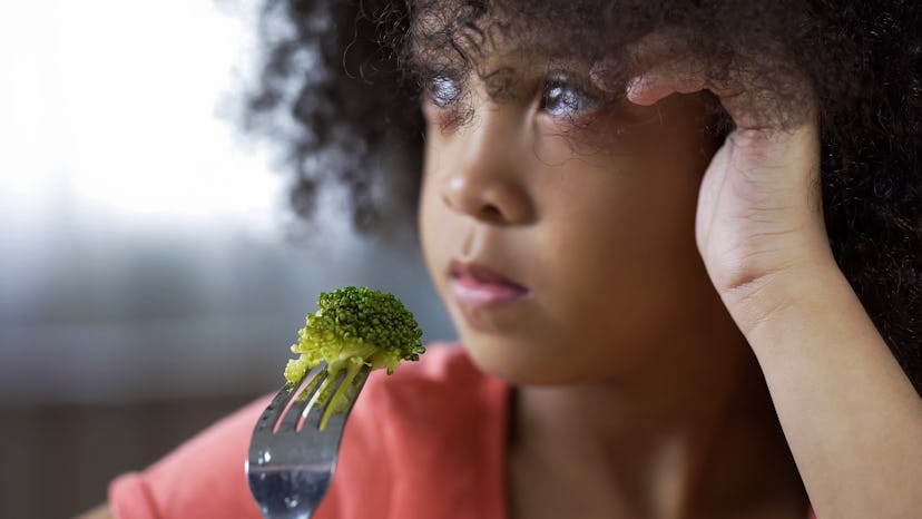 Little girl holding fork with piece of broccoli on it.