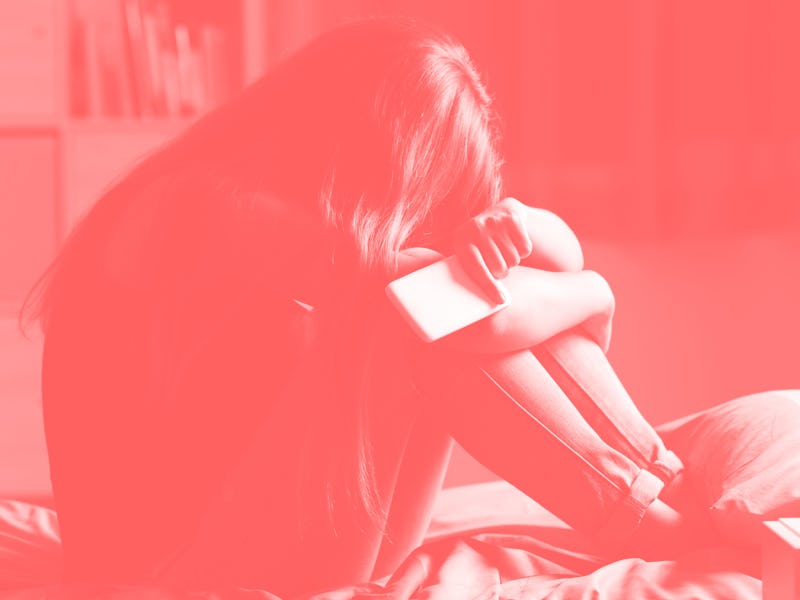 Single sad teen holding a mobile phone lamenting sitting on the bed in her bedroom with a dark light...