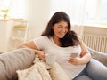 Beautiful cute young plus size female with loose dark hair enjoying cappuccino and surfing internet ...
