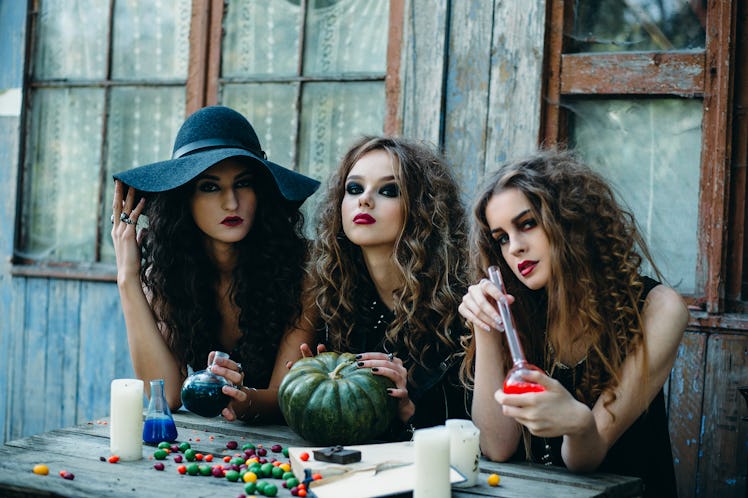 three witches are sitting at the table and prepared the potion on the eve of Halloween