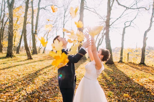 The autumn composition of the happy newlyweds throwing up the yellowed leaves in the park.