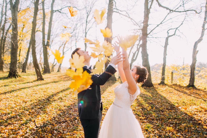 The autumn composition of the happy newlyweds throwing up the yellowed leaves in the park.