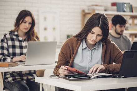 Pretty caucasian high school student reading a book at classroom.