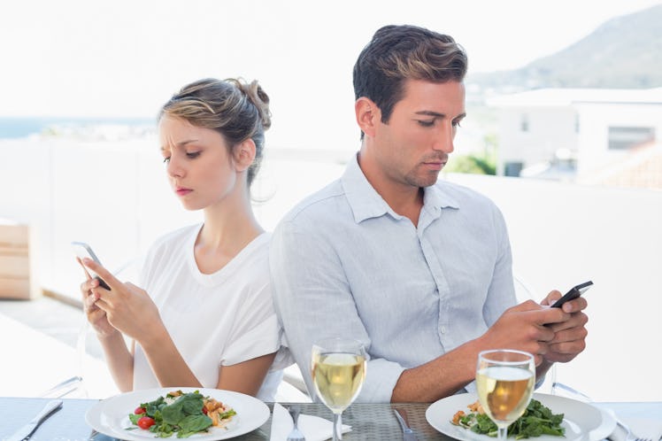 Concentrated young couple text messaging at food table