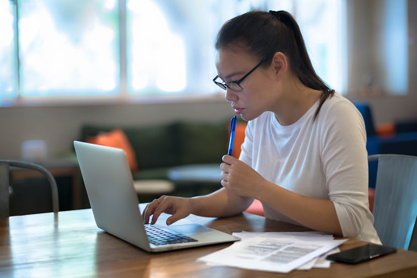 A young women doing work on her laptop computer at home.