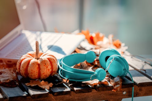 Orange pumpkin, headphones and leaves near laptop computer on a table. Autumn season time