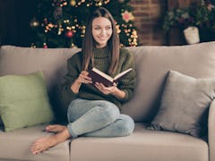 Full body photo of positive cheerful girl sit cozy divan cross her legs read christmas story imagine...