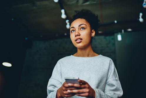 Pensive african american woman thinking about idea for blog holding mobile phone, thoughtful dark sk...