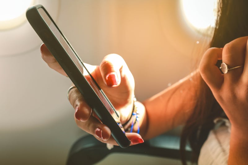 Girl’ with a phone in her hand sitting on the airplane.