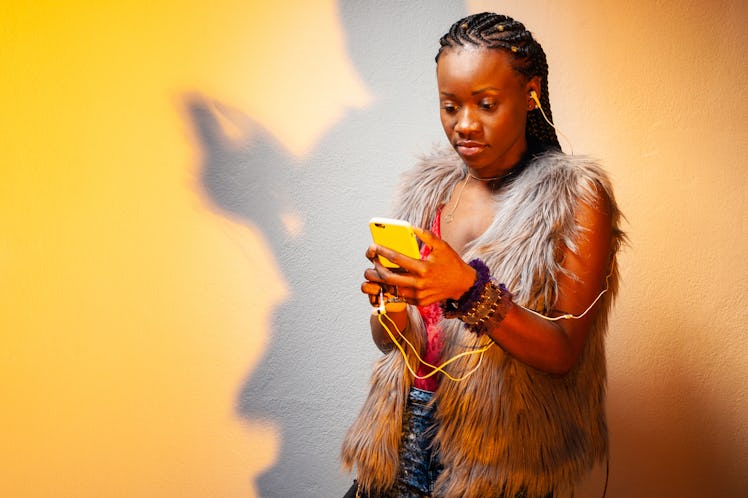 Black girl is listening to music. The girl in the headphones looks at the phone. African American wo...