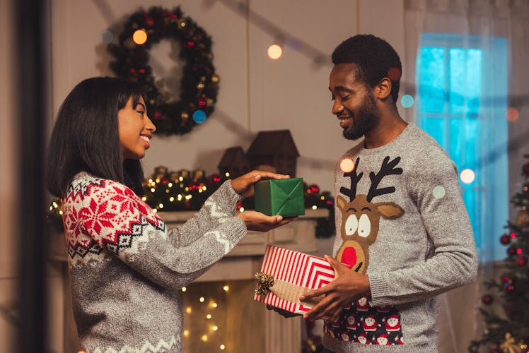 smiling african american couple presenting gifts to each other while celebrating christmas at home