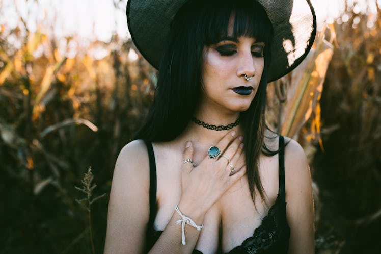Halloween costume witch girl portrait with close eyes in a cornfield at sunset. Beautiful sad and se...