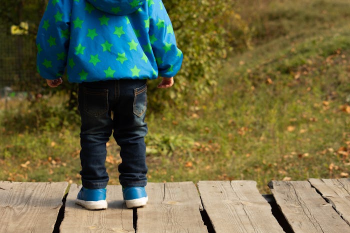 Child back side, blue shoes, clothes with gold stars, wood boards, green background