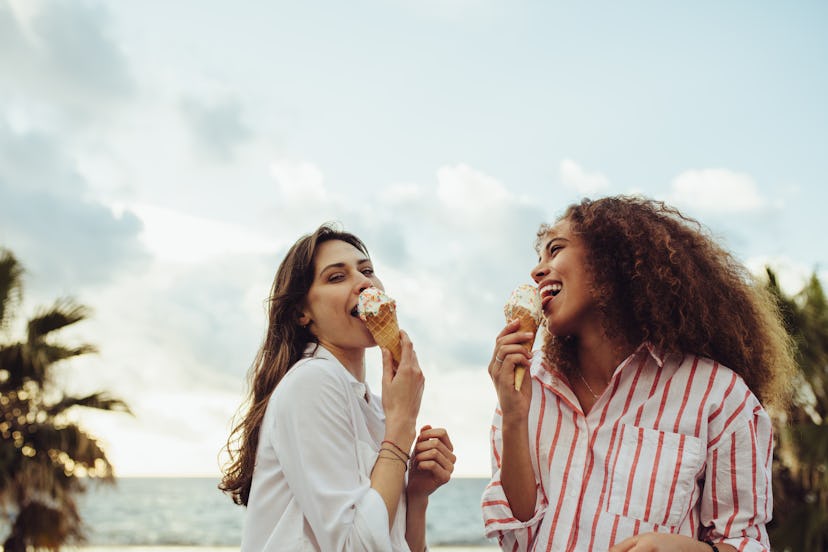 Two female friends licking the ice cream cone, disconnecting from technology on vacation