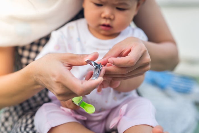 baby is cut fingernails by her mother. she concentrate at her nail.