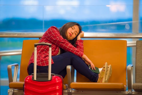 lifestyle portrait of young pretty tired and exhausted Asian Korean tourist woman in airport sleepin...