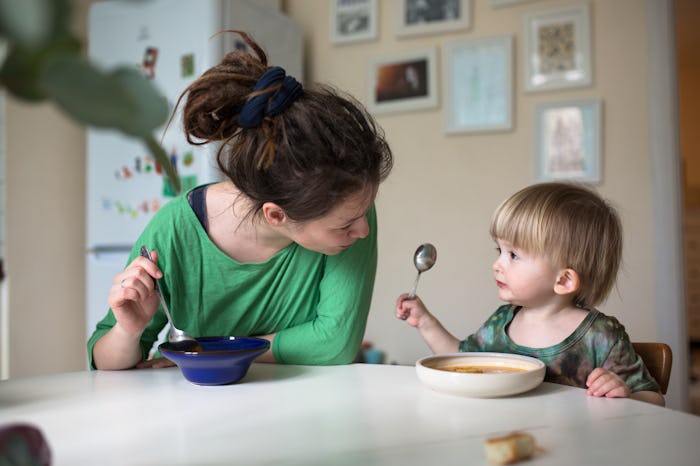 Mother with her baby eating soup in the bright kitchen at home, real interior, Mom with dreadlocks,...