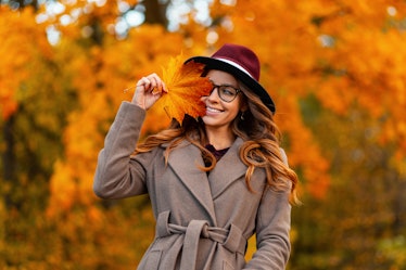 Happy trendy young woman in glasses in a vintage hat in an elegant coat poses with an orange-yellow ...