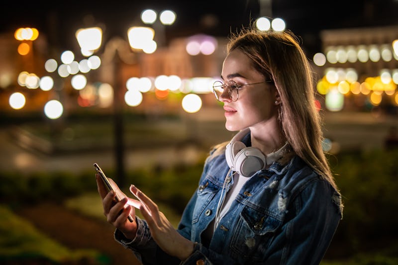 Young Caucasian woman texting cell phone in city at night