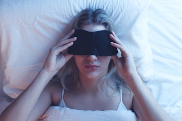 Sleeping girl in a sleep mask on an orthopedic pillow with night lighting, white bed linen.