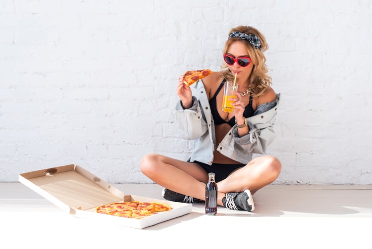 Young woman eating a piece of pizza, for which she'll need some pizza Instagram captions.