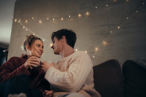 Cozy couple sitting on sofa and having coffee together. Man and woman relaxing on couch drinking cof...