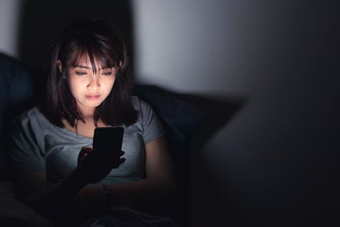 Woman using mobile phone on the bed in dark room.