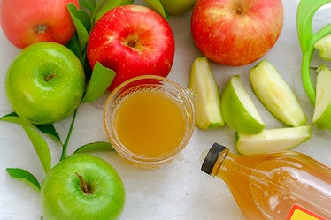 Apple cider vinegar in a glass cup in the middle of red and green apples with the bottle near by. Dr...