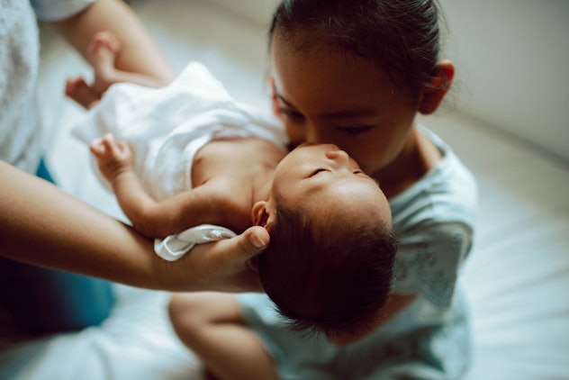 Mother teaches daughter how to hold a baby.