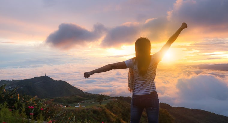 Person standing on mountain top as sun rises Person standing on mountain top as sun rises