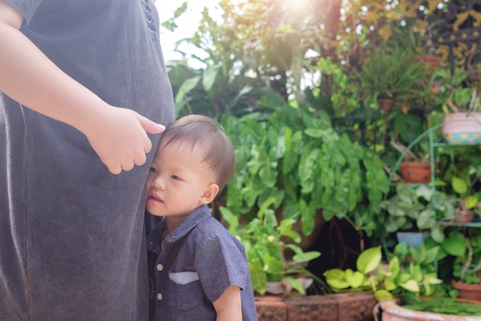 A toddler boy leans up against his pregnant mom's belly