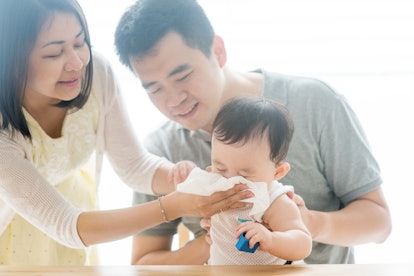 Mother wipes baby nose with tissue paper. Asian family spending quality time at home, living lifesty...