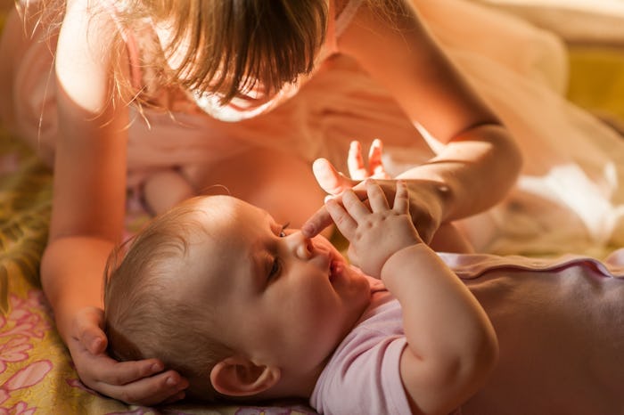 The baby is lying on her back and looks with a smile up at her sister. The older sister  presses the...