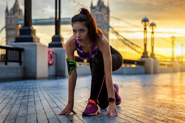 Pretty female athelete in starting position ready to do her workout during sunrise in an urban city