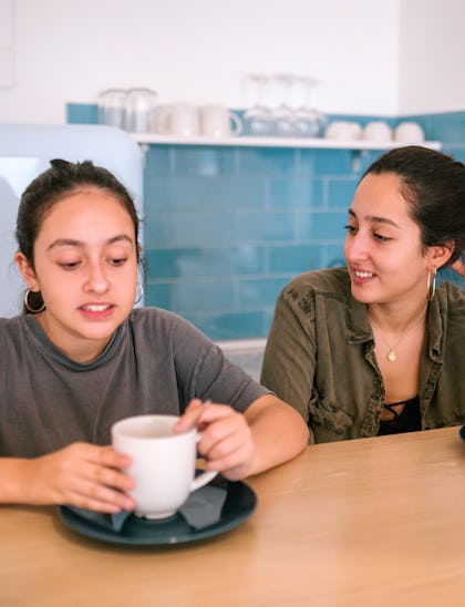 Teen sisters talking while they are having breakfast in the kitchen