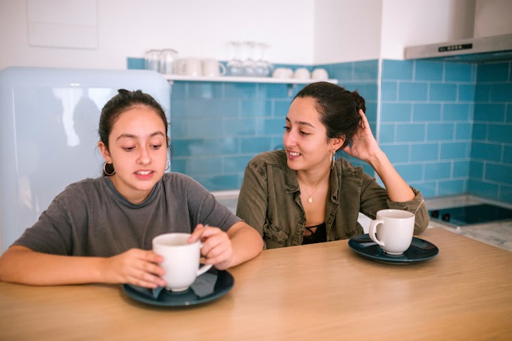 Teen sisters talking while they are having breakfast in the kitchen