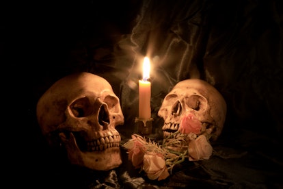 Two Human Skulls and dry flowers with light candle in dim valentines night on old wooden table / Sti...