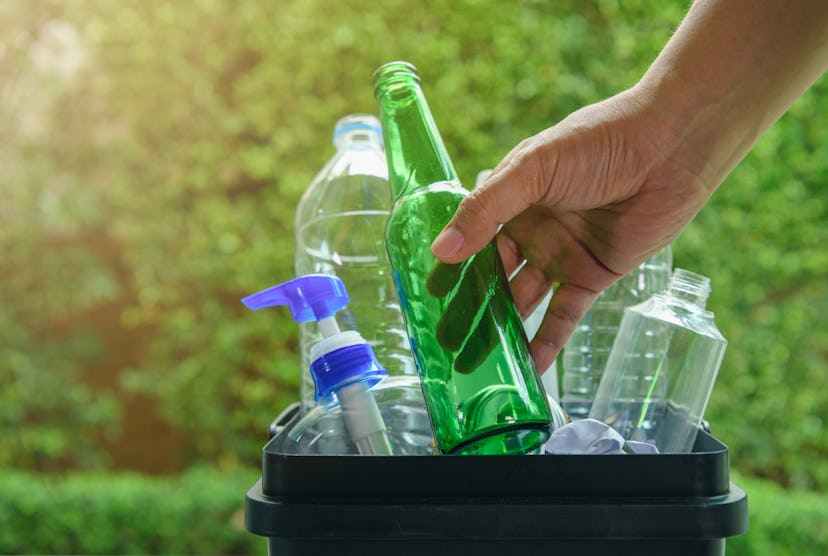 Close up hand dropping plastic and glass bottle into the bin for separating recycle materials from t...