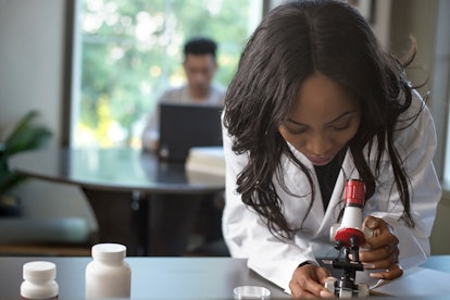 Female scientist in a lab coat researching with her male coed med school student in a campus laborat...
