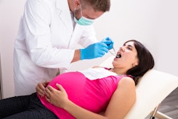 A Male Dentist Treating Teeth Of Young Pregnant Woman Patient Lying In Clinic