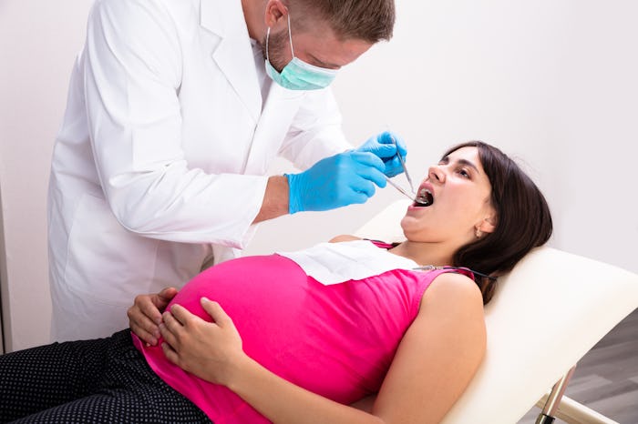 A Male Dentist Treating Teeth Of Young Pregnant Woman Patient Lying In Clinic