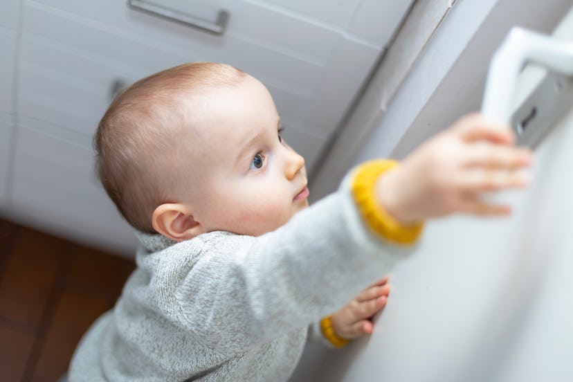 A little cute boy wants to open a door in the room. Portrait of a baby trying to reach a door-handle...