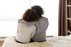 Rear back view black mother and daughter embrace sitting on bed at home, older sister consoling youn...