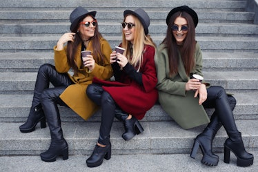 Stylish girls with unusual makeup in trendy coats, scarves, hats and leather shoes on the stairs to ...