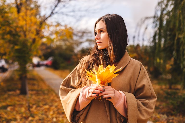 Cheerful sad girl with long brown hair wearing autumn beige coat, walking at the park. Autumn walk. ...